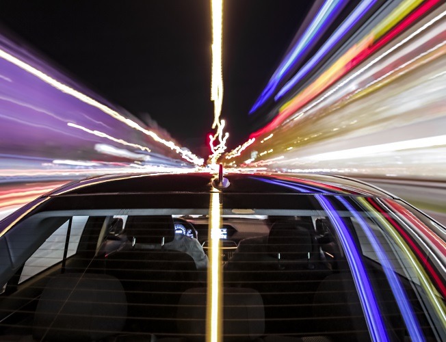 Ein schwarzes Auto mit bunten Reflexionen fährt auf einer Straße