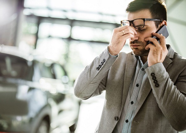 Geschäftsmann hat Kopfschmerzen, während er auf dem Handy in einem Auto-Showroom spricht